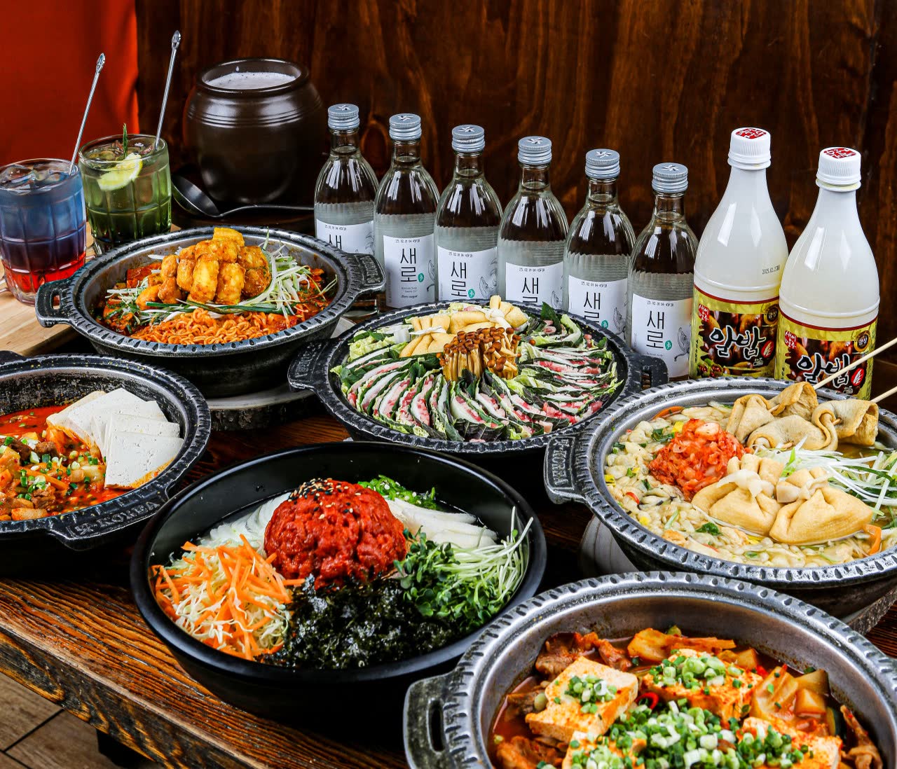 소주병과 막걸리병을 뒤에 늘어놓고 전골, 전, 육회비빔밥, 짜글이를 함께 차린 상차림