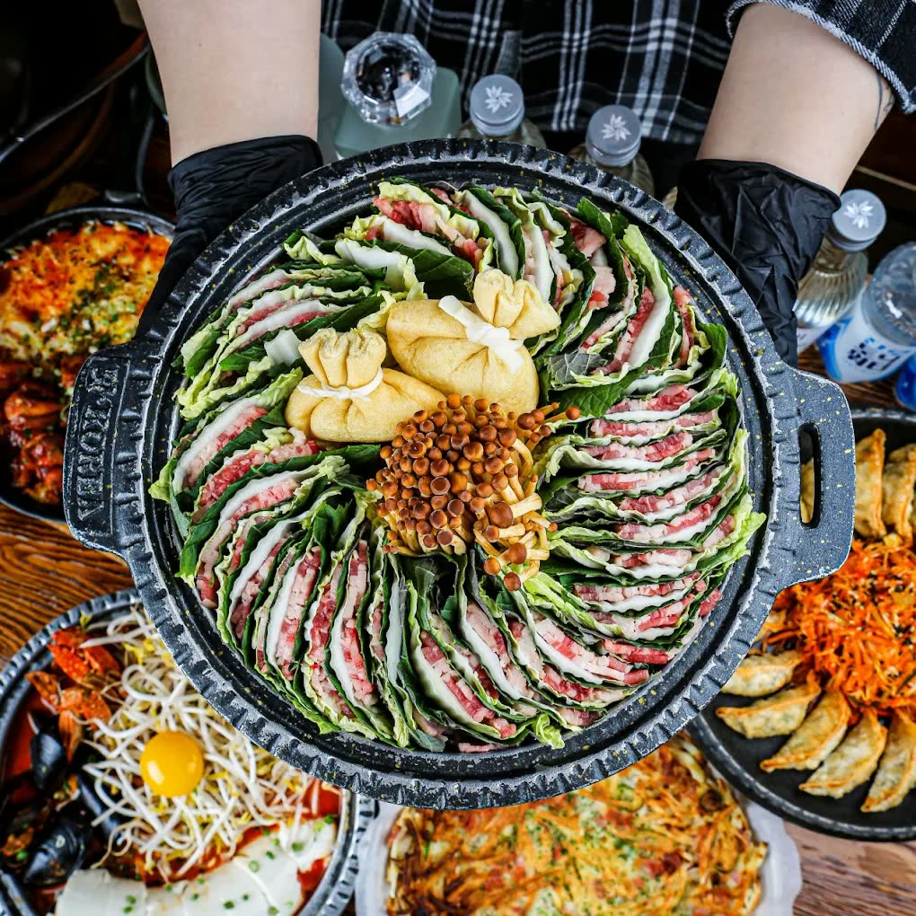 밀푀유나베를 위에서 본 모습 — 소고기와 배춧잎, 깻잎을 겹겹이 세워 둥글게 채우고 가운데에 팽이버섯과 만두를 올렸다