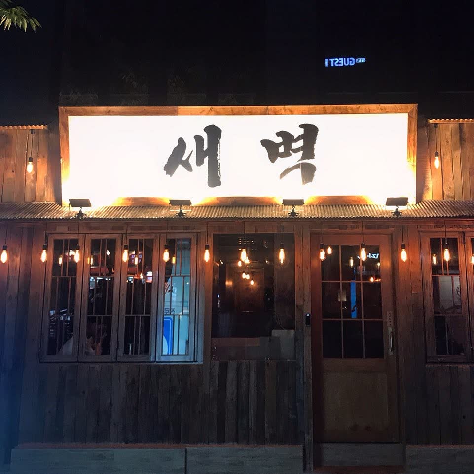 불을 밝힌 ‘새벽’ 간판과 그 아래 에디슨 전구가 늘어선 목조 출입구를 가까이에서 본 모습